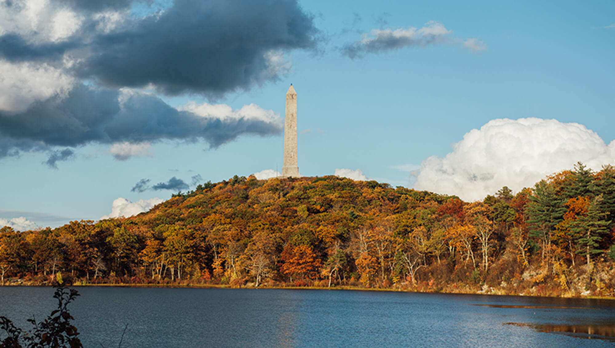 Hikes at High Point State Park. Scenic view of a lake in front of a mountain covered with trees and a watch tower on top.